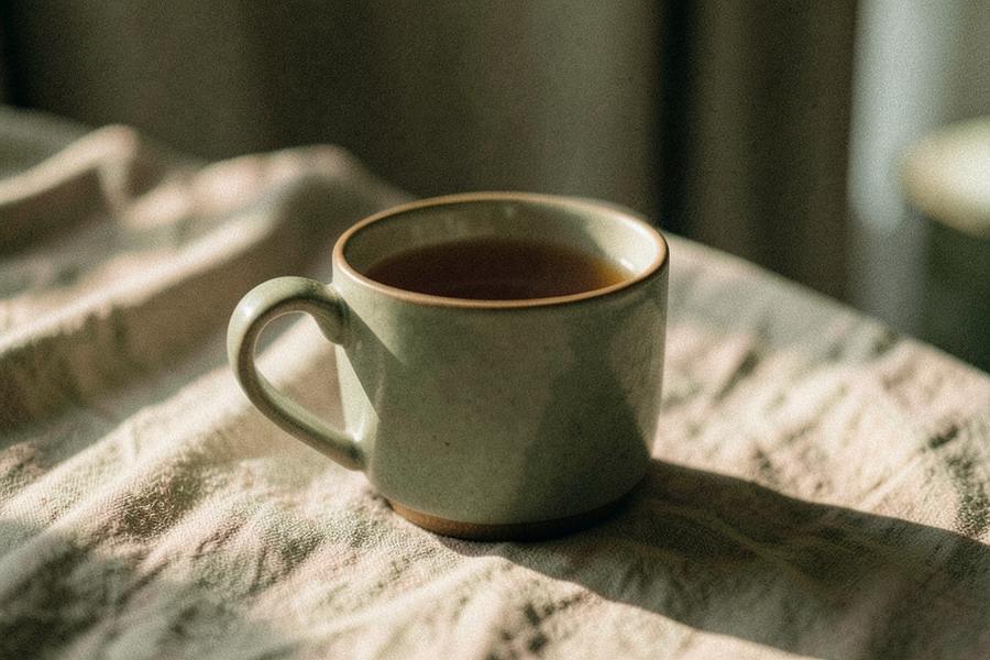 A ceramic mug of tea resting on a linen tablecloth in warm morning light